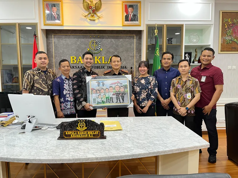 Enam pegawai kejaksaan di ruang kerja berlambang Garuda memegang karikatur kelompok berbingkai.