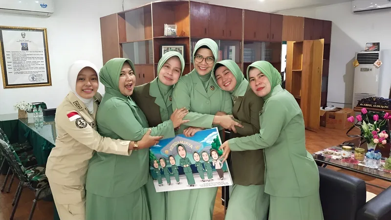 Lima perempuan berseragam hijau berangkulan sambil memegang karikatur kelompok berbingkai.