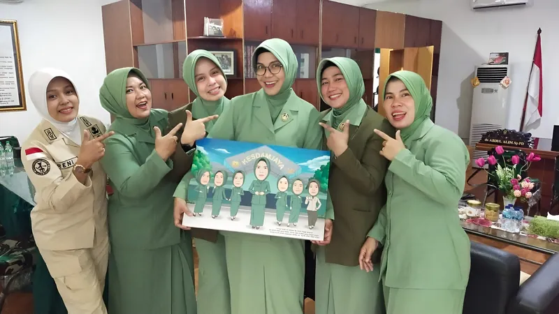 Lima perempuan berseragam hijau menunjuk karikatur kelompok berbingkai yang dipegang bersama.