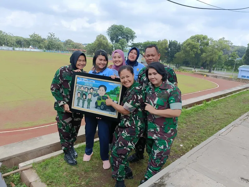 Enam anggota TNI berseragam loreng berfoto di tepi lapangan sambil memegang karikatur kelompok berbingkai.