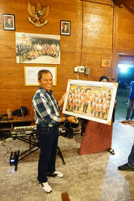 Seorang pria memegang karikatur kelompok berbingkai di ruang berdinding kayu.