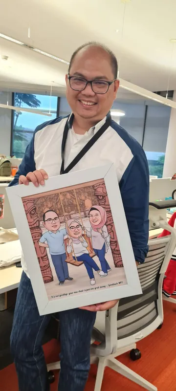 Pria berkacamata memegang karikatur keluarga berbingkai di ruang kerjanya.