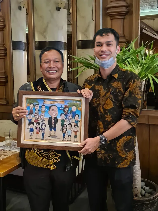 Dua pria berbatik berdiri berdampingan memegang karikatur kelompok berbingkai.