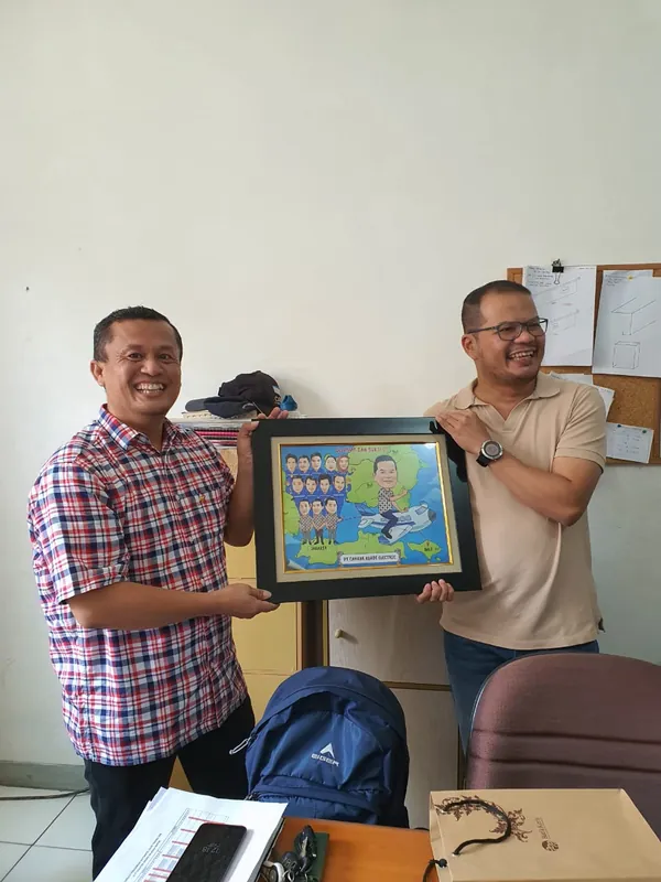Dua rekan kerja memegang karikatur berbingkai bersama di ruang kantor.