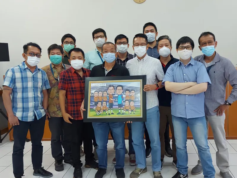 Rekan kerja bermasker berfoto bersama memegang karikatur kelompok berbingkai.