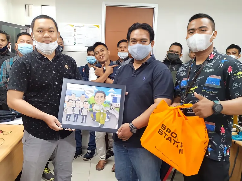 Penyerahan karikatur berbingkai kepada rekan kerja di ruang kantor.