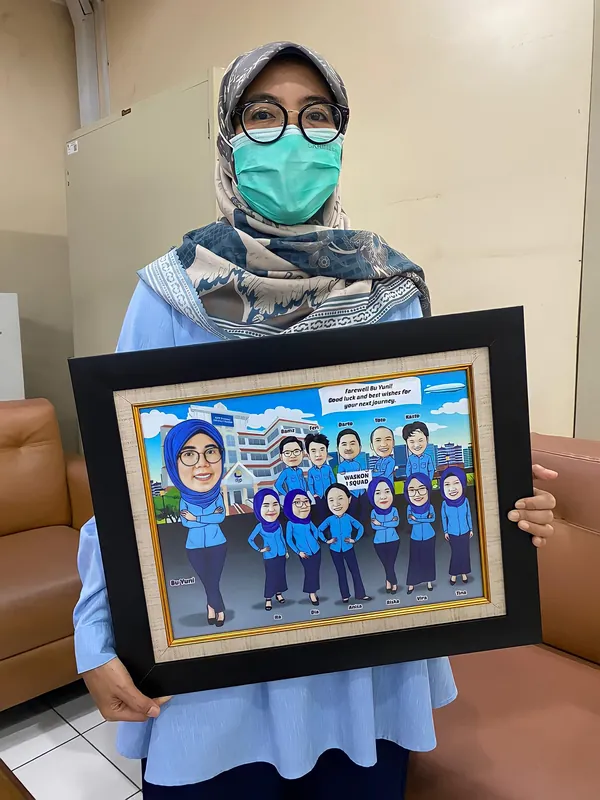Perempuan berhijab memegang karikatur kelompok berbingkai di ruang kerja.