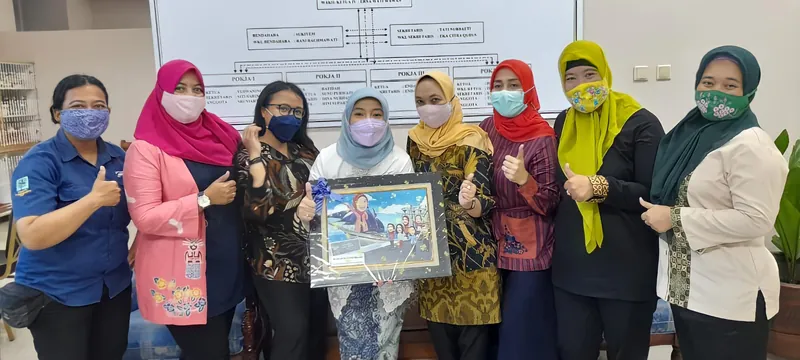 Sekelompok perempuan bermasker memegang karikatur kelompok berbingkai di ruang kerja.