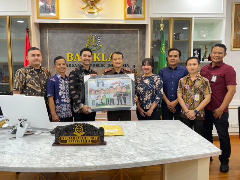 Tujuh pegawai kejaksaan berdiri di ruang kerja memegang karikatur kelompok berbingkai.