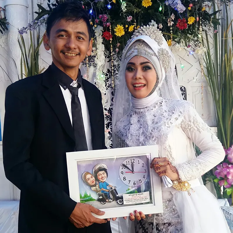 Sepasang pengantin memegang karikatur pernikahan berbingkai di pelaminan.