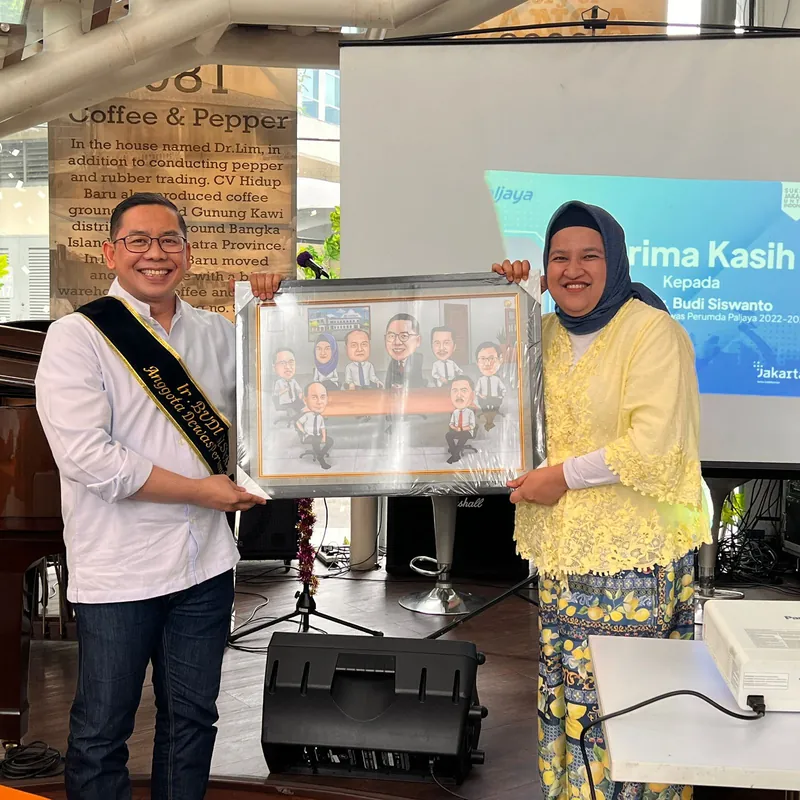 Penyerahan karikatur berbingkai di atas panggung acara terima kasih kantor.