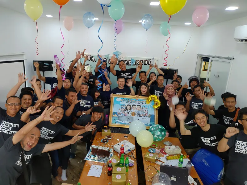 Karyawan merayakan penyerahan karikatur kelompok berbingkai di ruang kerja berhias balon.
