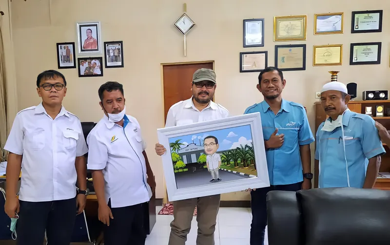 Lima pegawai berseragam putih memegang karikatur berbingkai di ruang kerja.