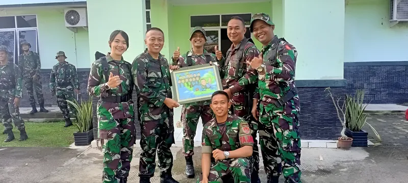 Anggota TNI berseragam loreng memegang karikatur kelompok berbingkai di ruang kantor.