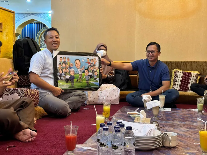 Rekan kerja duduk lesehan memegang karikatur kelompok berbingkai.