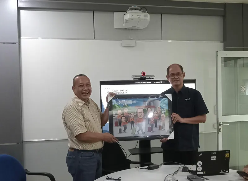 Dua pria memegang karikatur kelompok berbingkai di ruang rapat berlayar besar.