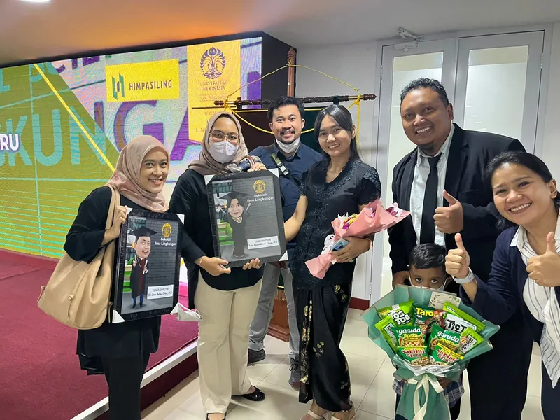 Sekelompok rekan kerja memegang karikatur berbingkai dan buket bunga di lobi kantor.