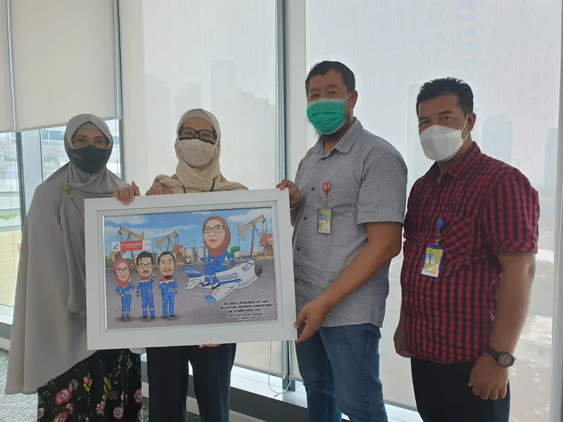 Empat rekan kerja memegang karikatur kelompok berbingkai di ruang kantor.