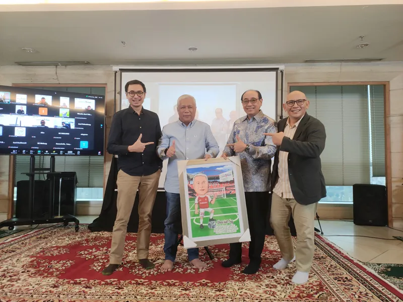 Empat pria memegang karikatur berbingkai di ruang rapat berkarpet merah.