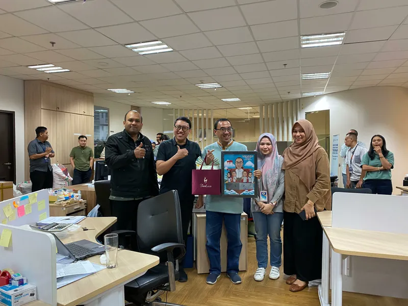 Rekan kerja berkumpul di ruang kerja memegang karikatur kelompok berbingkai.