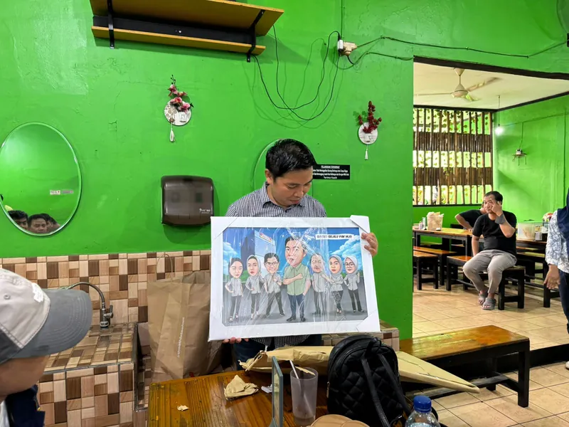 Seorang pria memegang karikatur kelompok berbingkai di ruang berdinding hijau.