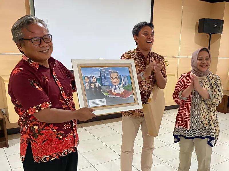 Tiga orang memegang karikatur berbingkai bersama di ruang acara kantor.