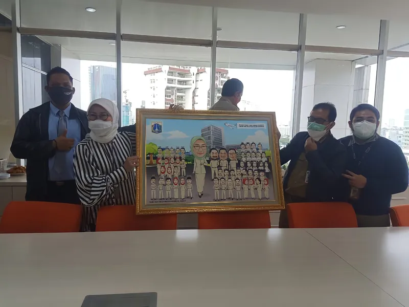 Rekan kerja memegang karikatur kelompok berbingkai di ruang kantor berjendela besar.