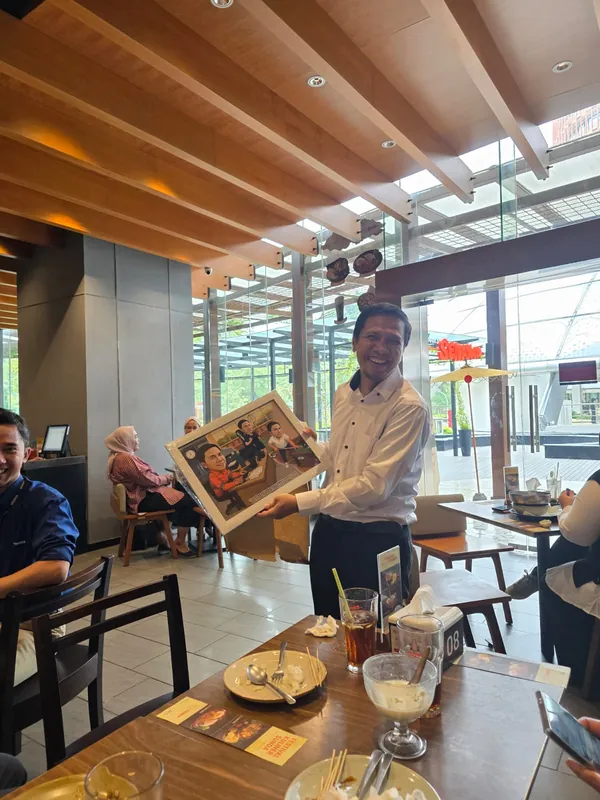 Dua pria memegang karikatur berbingkai di kafe kantor.