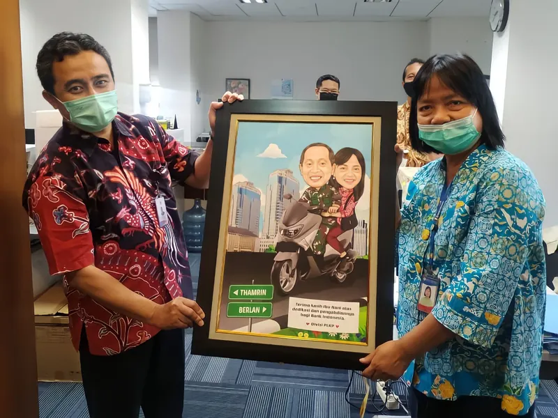 Seorang pria berbatik merah dan rekan perempuannya memegang karikatur berbingkai bertema motor.