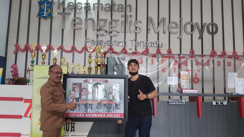 Dua pria memegang karikatur kelompok berbingkai di lobi kantor kecamatan.