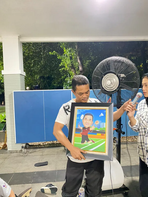 Seorang pria memegang karikatur berbingkai bertema olahraga di ruang kerja.