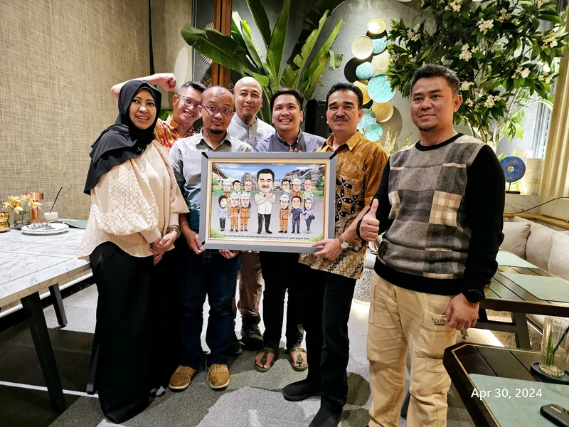 Rekan kerja berkumpul memegang karikatur kelompok berbingkai di ruang acara.