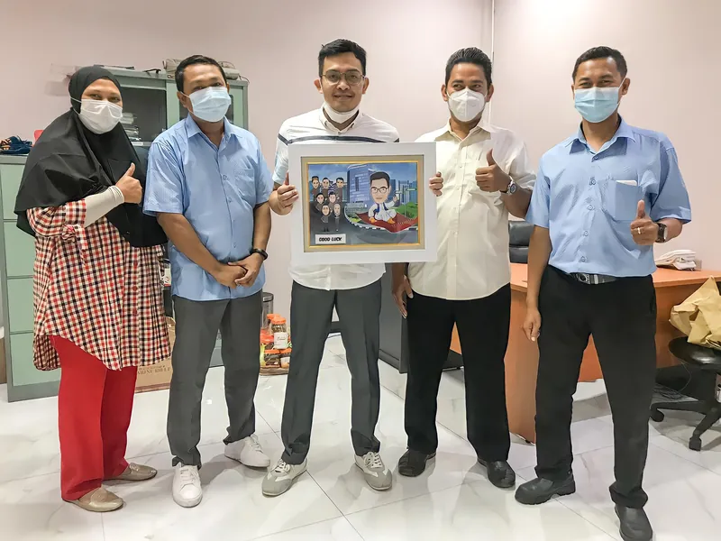 Lima rekan kerja memegang karikatur berbingkai di ruang kantor.