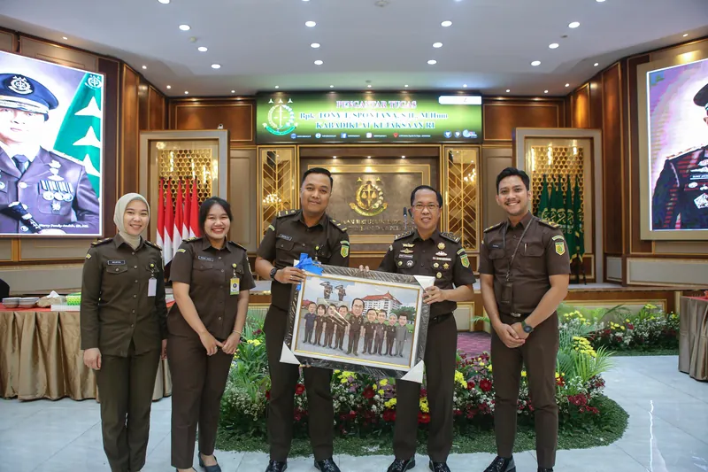 Penyerahan karikatur kelompok berbingkai antara pejabat kejaksaan di ruang resmi.
