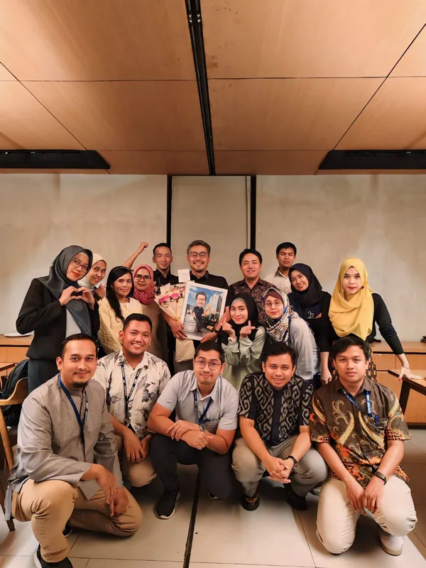 Rekan kerja berfoto bersama di ruang kantor memegang karikatur kelompok berbingkai.