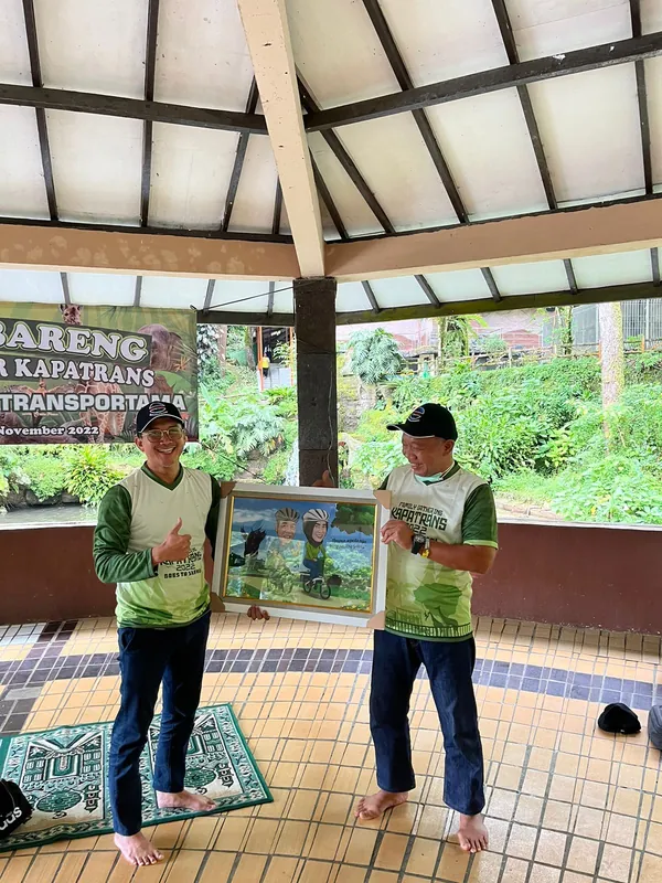 Dua pria memegang karikatur berbingkai di saung kayu.