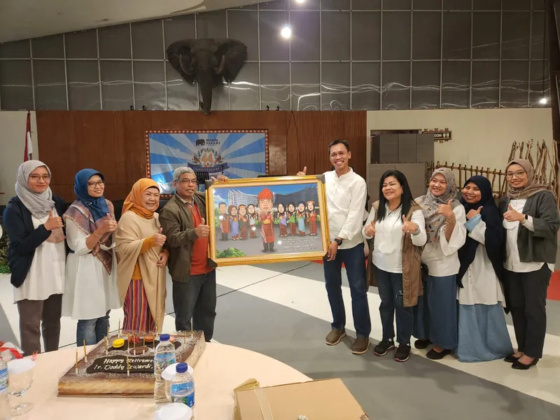 Rekan kerja berkumpul memegang karikatur kelompok berbingkai di ruang acara.