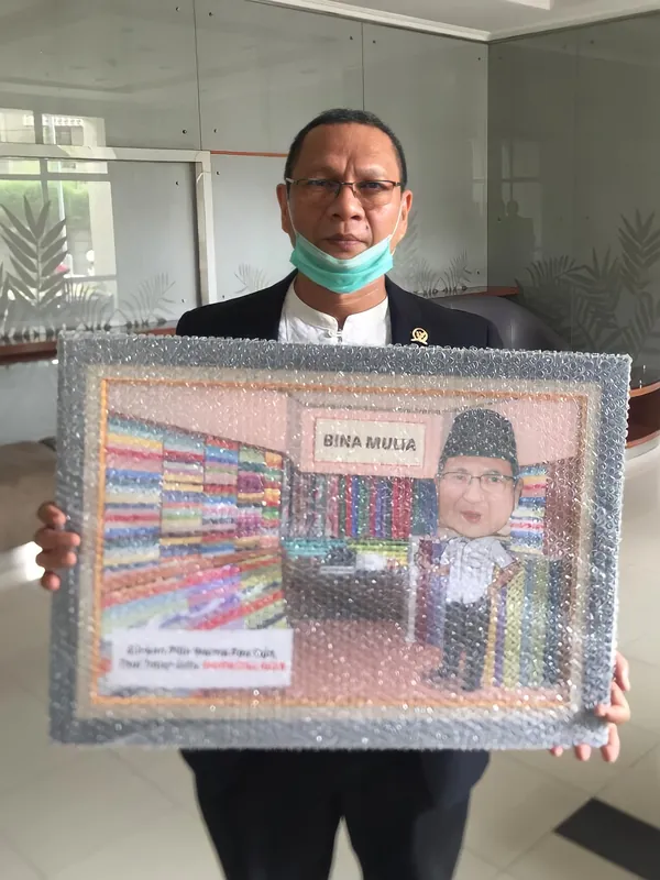 Seorang pria memegang karikatur berbingkai berhias manik di ruang kantor.
