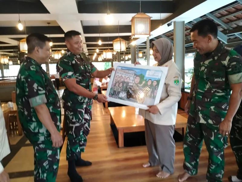 Anggota TNI menyerahkan karikatur kelompok berbingkai kepada rekannya di restoran.
