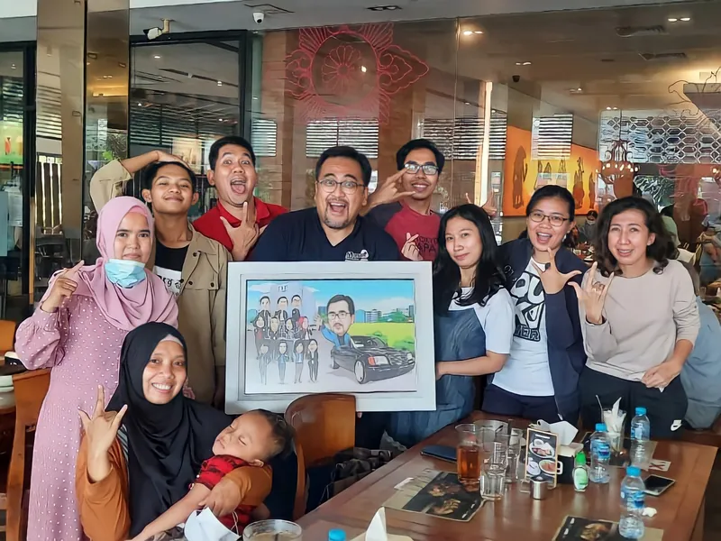 Rekan kerja dan keluarga berkumpul di restoran memegang karikatur kelompok berbingkai.