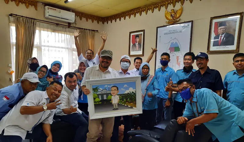 Karyawan berseragam biru berkumpul memegang karikatur kelompok berbingkai.