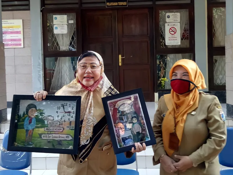 Dua perempuan memegang dua karikatur berbingkai di lobi kantor.