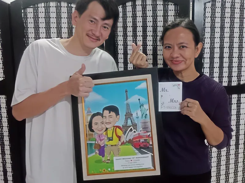 Dua orang memegang karikatur pasangan berbingkai bertema perjalanan ke Paris.
