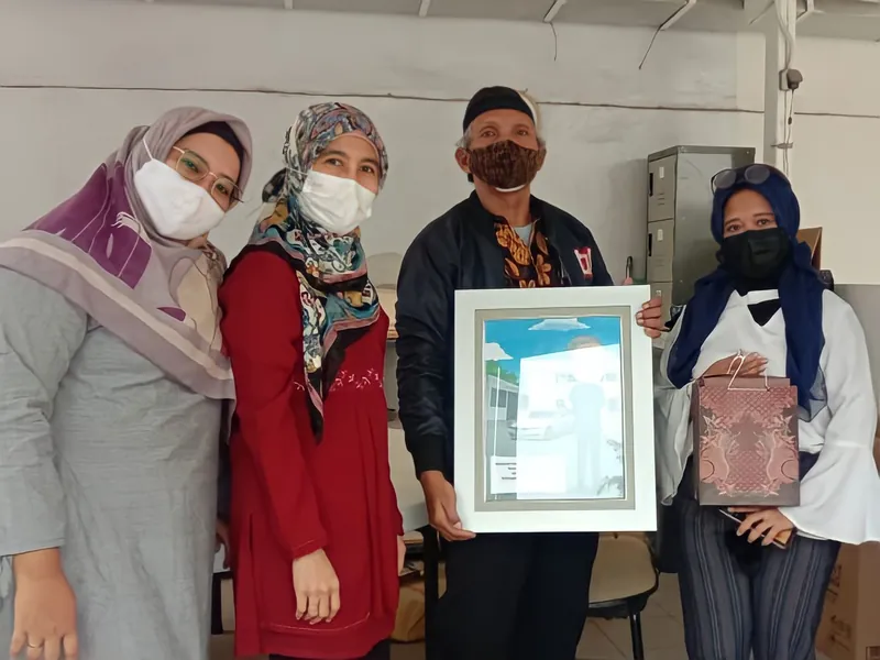 Empat rekan kerja memegang karikatur berbingkai di ruang kantor.