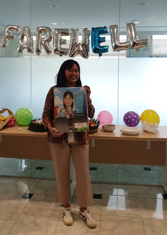 Seorang perempuan memegang karikatur berbingkai di ruang berhias balon perpisahan.