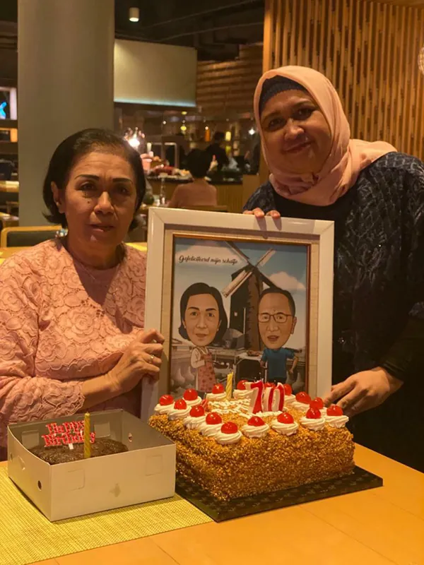 Dua perempuan memegang karikatur pasangan berbingkai di samping kue.