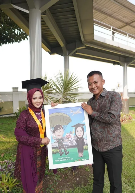 Seorang wisudawati dan rekannya memegang karikatur wisuda berbingkai.