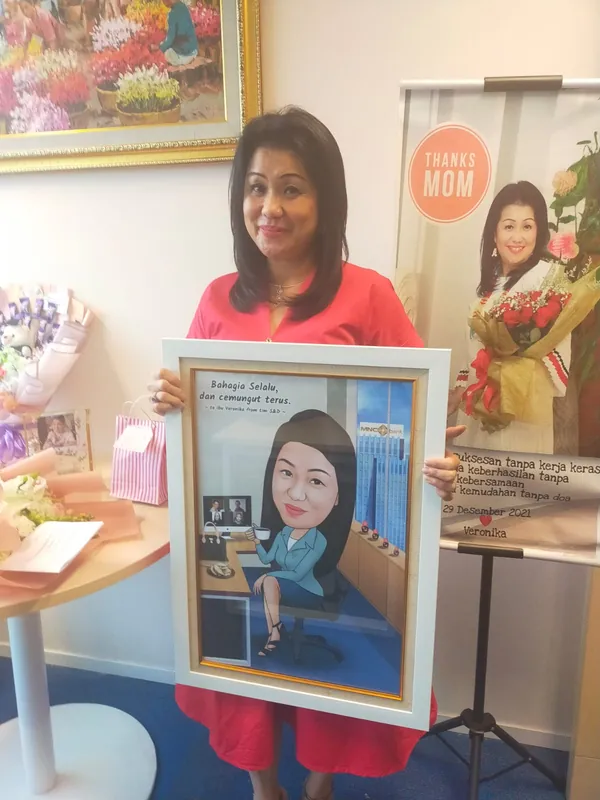 Seorang perempuan memegang karikatur berbingkai di ruang acara berhias bunga.