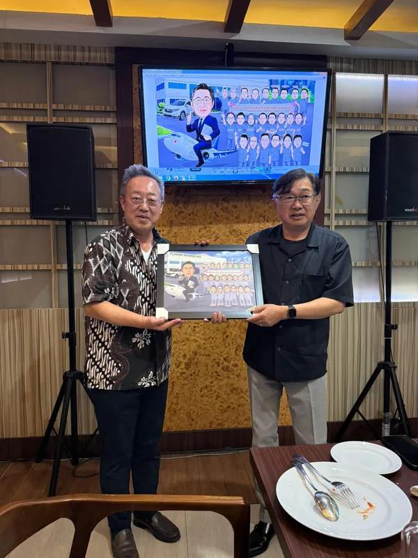 Dua pria memegang karikatur kelompok berbingkai di ruang acara.