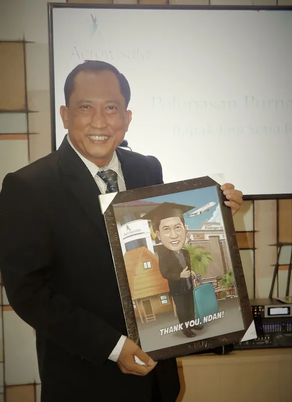 Seorang pria berjas memegang karikatur berbingkai bertema perpisahan.